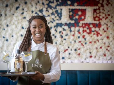 HYDE Hotel | Galway | Female wait staff holding HYDE Gin in front of HYDE Bar flower wall